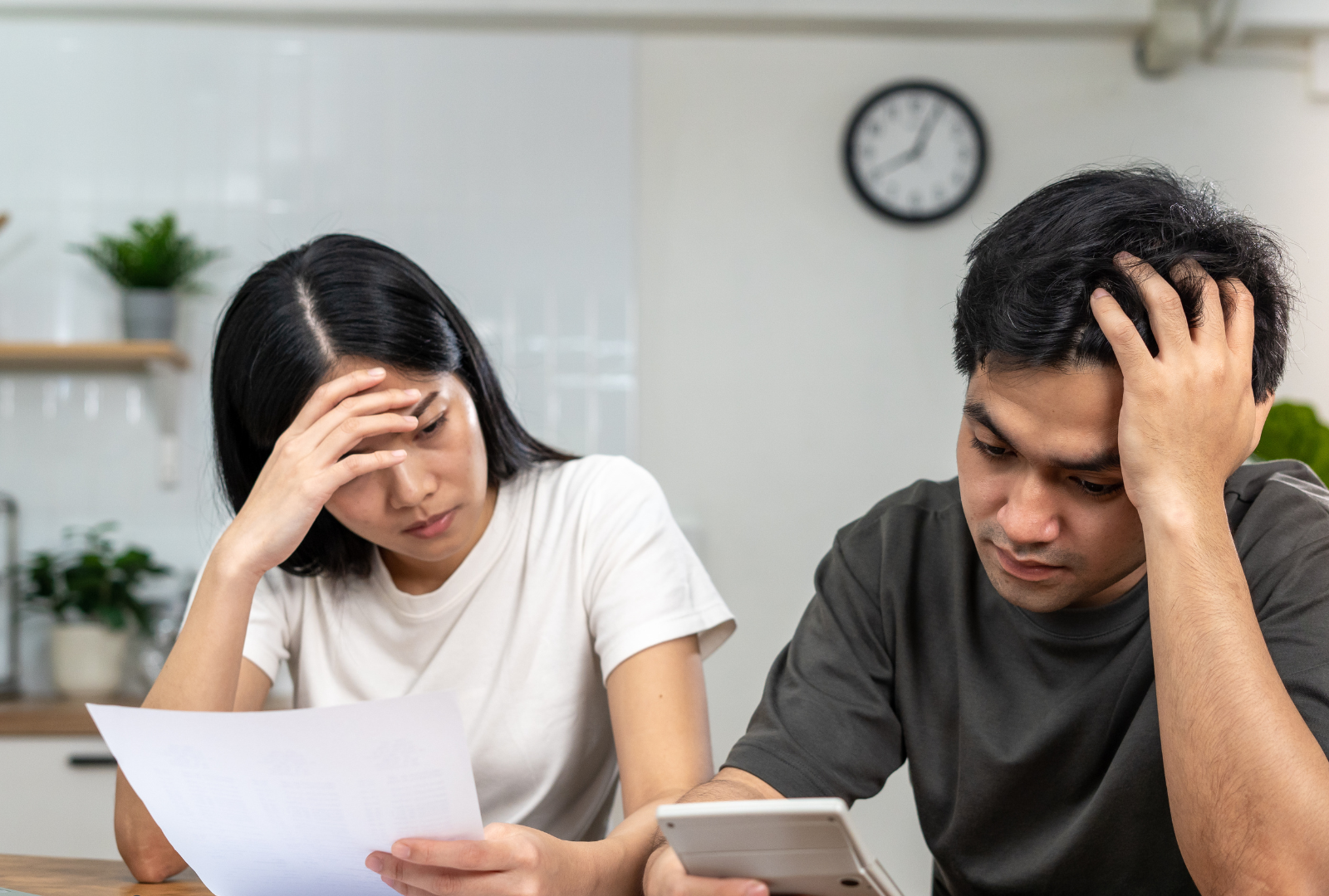 Pareja sentada en la cocina revisando facturas y una calculadora, con gesto de preocupación, reflejando la tensión de llegar just@ a final de mes a pesar de tener un buen sueldo.