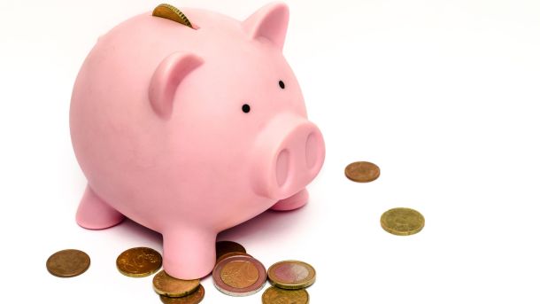 Hucha con forma de cerdito con monedas a su alrededor. Definición fácil de Ahorro